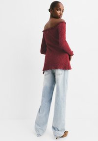 Top bordeaux a spalle scoperte con finiture a scalloped, abbinato a jeans a gamba larga azzurri, indossato con scarpe con tacco marroni.