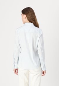 Camicia a maniche lunghe di colore blu chiaro con righe verticali bianche, colletto e polsini abbottonati. Tessuto morbido con una vestibilità leggermente rilassata.