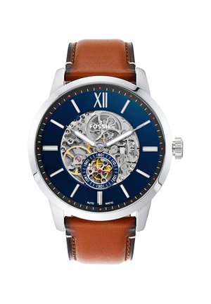 Montre ronde argentée Fossil avec cadran bleu, engrenages mécaniques exposés, index blancs et bracelet en cuir marron.