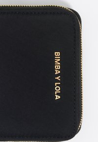 Cartera de textil negra con cremallera dorada y logotipo en relieve "BIMBA Y LOLA". Superficie lisa, forma rectangular con bordes redondeados.
