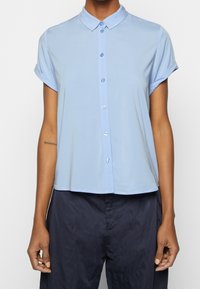 Chemise bleu clair à manches courtes avec col, manches retroussées et coupe décontractée, confectionnée dans un tissu lisse et léger.