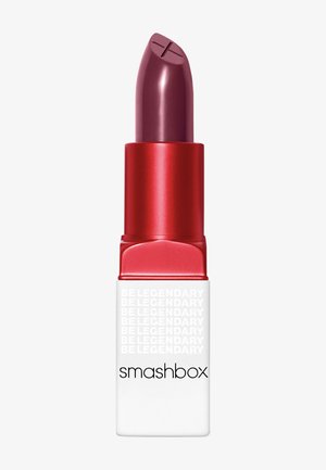 Rouge à lèvres Smashbox avec un bullet bordeaux, logé dans un tube rectangulaire rouge et blanc. Affiche le texte "BE LEGENDARY" sur le côté.
