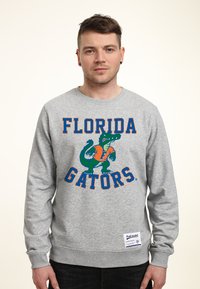 Šedá mikina s kulatým výstřihem, na které je nápis 'FLORIDA GATORS' v oranžové barvě, s grafikou aligátora v zelené a modré, a štítkem v pravém dolním rohu.