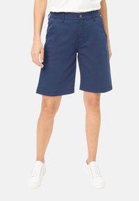 Pantaloni corti blu navy realizzati in un tessuto leggero, con una vestibilità comoda, tasche frontali e orlo arrotolato. Abbinati a sneaker bianche.