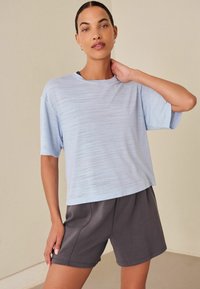 T-shirt azzurro chiaro a maniche corte, con texture, abbinato a pantaloni atletici grigio scuro. Entrambi realizzati in materiali morbidi e traspiranti.