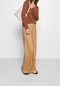 Rostfärgad stickad tröja med V-ringning, i kombination med ljusbruna linnebyxor med vida ben. Accessoarer med en vävd krämfärgad väska och svarta sandaler.