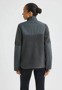 Fleece takki, jossa on tummanharmaa teksturoitu vartalo ja sileät harmaat hihat. Ominaisuuksiin kuuluu korkea kaulus ja rento istuvuus.