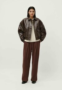 Veste en cuir marron courte avec un col, des poches avant et des poignets élastiques, assortie à un pantalon large de couleur rouge foncé et des chaussures noires.