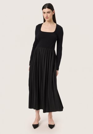 Black dress with a fitted long-sleeve top and a pleated skirt. Features a square neckline, smooth texture, and ankle-length design.