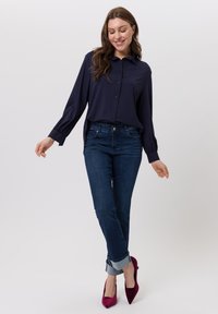 Marineblaues langärmliges Hemd mit Knöpfen und entspannter Passform, kombiniert mit dunkelblauen Jeans, die am Saum hochgekrempelt sind, und fuchsiafarbenen, spitz zulaufenden High Heels.