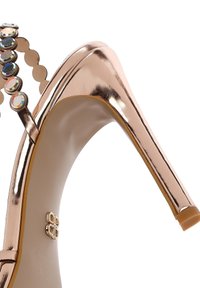 Rose gold metallic high-heeled sandal with gem-encrusted ankle straps and a thin stiletto heel on a white background.
