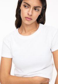 Witte T-shirt met korte mouwen, voorzien van een ribbelstructuur en een ronde halslijn. Het model toont een lichte overlapping van de stof bij de taille.