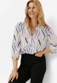 Langärmlige Bluse aus leichtem, gemustertem Stoff mit geometrischen Formen in Pink, Blau, Schwarz und Creme, mit Kragen und Knopfverschluss.