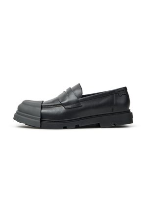 Mocassin en cuir noir avec semelle épaisse en caoutchouc et embout en caoutchouc prolongé couvrant l'avant de la chaussure.
