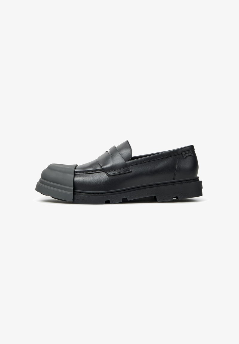 Mocassin en cuir noir avec semelle épaisse en caoutchouc et embout en caoutchouc prolongé couvrant l'avant de la chaussure.