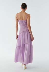 Lavendelfarbenes Maxikleid mit verstellbaren Spaghettiträgern und gestuftem Design. Leichter Stoff mit dezenter Textur und dekorativen Steppnähten.