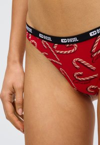 Sous-vêtements rouges avec un motif de cannes en sucre d'orge. Ceinture élastique noire avec le logo "DIESEL", tissu lisse, coupe ajustée et taille mi-haute.