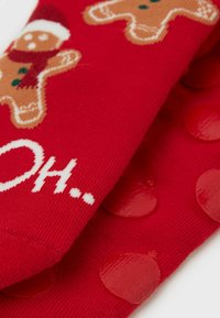 Červené ponožky s motivem perníčkových panáčků a nápisem „OH...“. Na spodní straně protiskluzové gumové tečky pro lepší přilnavost. Měkká textura.