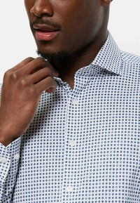 Weißes Hemd mit einem kleinen kreisförmigen blau-navy Muster, mit einem Button-Down-Kragen und weißen Knöpfen auf der Vorderseite.