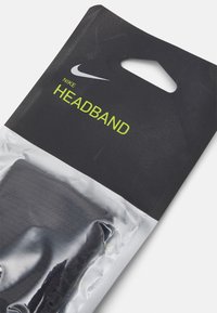 Un bandeau Nike emballé dans un plastique transparent avec un arrière-plan noir. Présente un logo Nike blanc et "HEADBAND" en texte vert fluo.