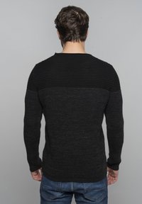 Maglione nero a maglia con sezione superiore a costine testurizzate. Maniche lunghe e fit aderente, abbinato a jeans in denim.