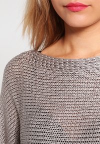 Pull en maille gris clair avec un motif ajouré, présentant un col large en forme de bateau et une texture douce, idéal pour le superposition.