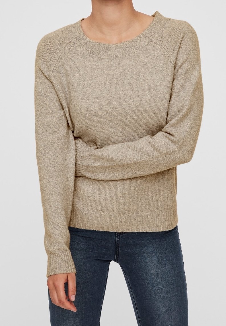 Beiger Strickpullover mit Raglanärmeln, rundem Ausschnitt und gerippten Bündchen. Weiche Textur mit subtilm Muster, kombiniert mit dunklen Jeans.