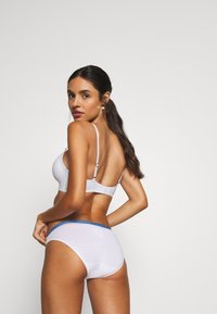 Ensemble de lingerie blanche comprenant un bralette avec des bretelles réglables et un short taille haute assorti, tous deux avec une texture douce et une taille en bleu.