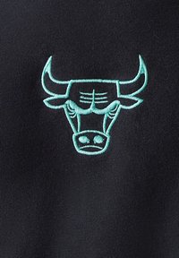 Μαύρο ύφασμα με πράσινο κεντητό λογότυπο κεφαλής ταύρου με επιβλητικά κέρατα, λεπτομερείς χαρακτηριστικά προσώπου και ομαλή υφή.