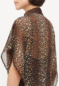 Kimono stil majica s uzorkom leoparda od prozirnog materijala, koja se ističe mješavinom narančastih i smeđih tonova s crnim detaljima i ovratnikom.