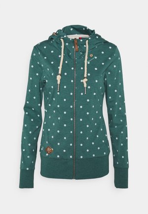 Green zip-up hoodie with white polka dots, cream rope drawstrings, and a small brown patch near the hem.