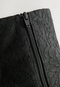 Černé krajkové boty s květinovým vzorem, s bočním zipem. Texturovaná tkanina s propracovanými detaily, kombinující hladké a vyvýšené prvky.