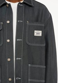 Donker denim jack met een kraag, zilveren drukknoopjes, twee voorzakken, witte stiksels en een merkenlabel op de linkerkant van de borstzak.