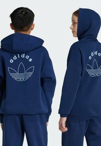 Las sudaderas con capucha de color azul marino presentan un gran logo blanco de Adidas y un diseño de hoja en la parte posterior. La tela es suave y tiene un corte relajado.