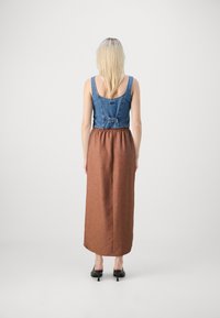Denim overdel med firkantet halsudskæring, der overgår til en brun, struktureret, gulvlængde nederdel. Har en bælte i taljen. Sorte hæle sko.
