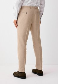 Pantalones de lino beige con corte recto, que cuentan con dos bolsillos traseros con cierres de botón y una cinturilla elástica.