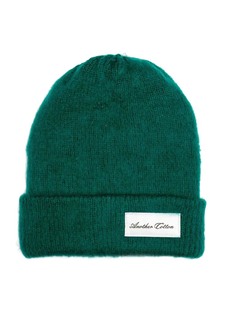 Žalias megztas kepurė nuo šalčio, pagaminta iš minkštos medžiagos su užlenktu kraštu. Šonėje yra balta etikete su juodu tekstu.