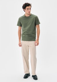 Tricou scurt olive cu mânecă scurtă, croială lejeră, guler rotund; asortat cu pantaloni drepți bej deschis și încălțăminte neagră.