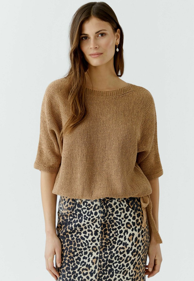 Brauner Strickpullover mit kurzen Ärmeln, kombiniert mit einem Rock im Leopardenmuster. Der Pullover hat einen runden Ausschnitt und eine lockere Passform.