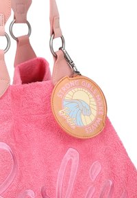 Roze badstof tote bag met een zachte textuur, voorzien van een leren label met de tekst "STERKE MEISJES MAKEN GOLVEN" en een zon- en golfafbeelding.