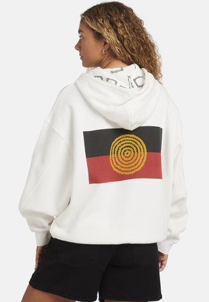Weißer Kapuzenpullover mit einem großen spiralförmigen Design in Gelb, Schwarz und Rot auf der Rückseite; hat ein gemustertes schwarzes Futter in der Kapuze.