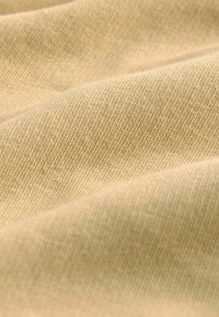 Beige stof med en fin, tekstureret vævning; glat overflade med subtil glans; draperet i bløde folder, der viser dybde og lysleg.