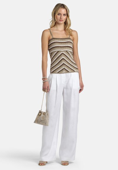 Femme portant un haut sans manches à rayures marron et blanc, un pantalon blanc à jambes larges, des sandales beige, tenant un sac à main à chaîne dorée et portant des bracelets.