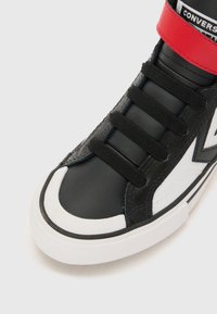 Musta nahkainen korkeavartinen tennari, jossa on valkoinen kärkikuvio, punainen nauha ja mustat nauhat. Kengässä on valkoinen logo sivulla ja teksturoitu pinta.