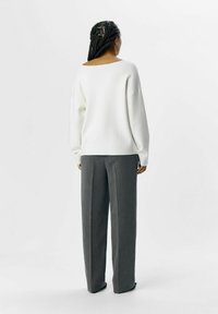 Witte, oversized trui met een brede halslijn en lange mouwen, gecombineerd met grijze, hoogopgetrokken, loszittende broek.