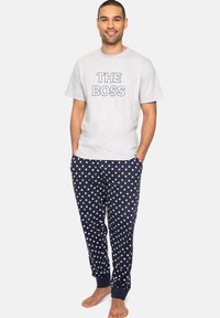 Graues kurzärmliges T-Shirt mit dem Aufdruck "THE BOSS" in Schwarz. Marineblaue Schlafanzughose mit weißen Sternmustern, an den Knöcheln umgeschlagen.