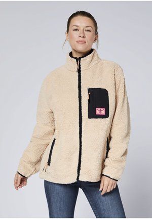 Fleece jacket in beige with black accents, featuring a high collar, zip closure, and a chest pocket with a pink logo patch.