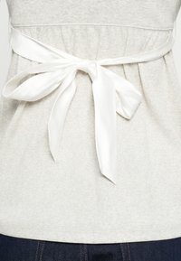 Ανοιχτό γκρι τοπ με υφή, διαθέτει σούρα στη μέση και λευκή σατέν �κορδέλα δεμένη σε φιόγκο στο πίσω μέρος.