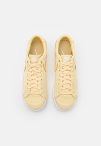 Gula canvas sneakers med rund tå, platta snören och en texturerad insida, med en vit Nike-logotyp på sidan.