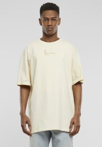 Light yellow oversized t-shirt with a round neckline and short sleeves, featuring a subtle beige logo at the center. Smooth cotton texture.